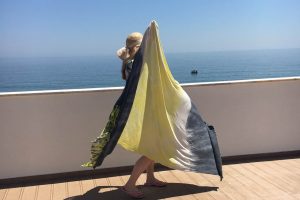 In Burgau, Algarve, wenige Meter von ihrem Casa Valeria und oberhalb des Strandes vom Fischerdorf Burgau, steht Edith steht Edith Wittkamp mit ihrem Lieblingstuch in gelb und grau, riesig ist es! Das Tuch ist von der fairen Marke für Yogakleidung, Milla Hamburg.