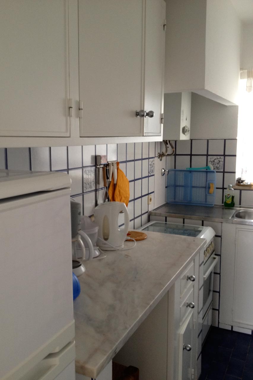 Die Küche im Casa Valéria sieht man auf diesem Bild. Links ist eine Küchenzeile in weiß mit einem Kühlschrank, Unter-und Oberschränken, daran schliesst der Herd mit Backofen und eine Spüle an. Die Küche hat ein Fenster und Tageslicht.