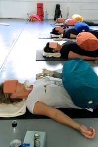Iyengar Yoga Workhop am Sonntag mit Edith Wittkamp.Hier liegen die Teilnehmer auf ihren Matten zum Entspannen. Auf ihrem Bauch ein längliches, dickes Kissen, auf den Augen sind Sandsäckchen damit die Augenmuskeln entspannen.